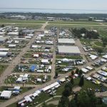 Low-level aerial view of AirVenture, looking down the main thoroughfare toward Boeing Plaza, with the flightline and runway 18/36 beyond. [Credit: LeRoy Cook]