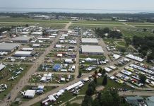 Low-level aerial view of AirVenture, looking down the main thoroughfare toward Boeing Plaza, with the flightline and runway 18/36 beyond. [Credit: LeRoy Cook]