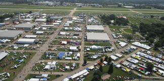 Low-level aerial view of AirVenture, looking down the main thoroughfare toward Boeing Plaza, with the flightline and runway 18/36 beyond. [Credit: LeRoy Cook]
