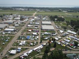 Low-level aerial view of AirVenture, looking down the main thoroughfare toward Boeing Plaza, with the flightline and runway 18/36 beyond. [Credit: LeRoy Cook]