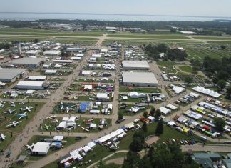 Low-level aerial view of AirVenture, looking down the main thoroughfare toward Boeing Plaza, with the flightline and runway 18/36 beyond. [Credit: LeRoy Cook]