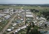 Low-level aerial view of AirVenture, looking down the main thoroughfare toward Boeing Plaza, with the flightline and runway 18/36 beyond. [Credit: LeRoy Cook]